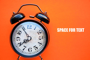 Old, vintage retro alarm clock on a bright orange background.