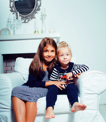 two cute sisters at home playing, little smiling girl in house interior on sofa, messing hair,...