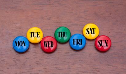 Close up weekly date on colorful button with wood background