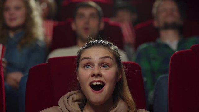 Zoom in closeup shot of young woman opening mouth being highly surprised and even shocked while watching film in cinema