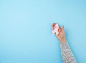 female hand holds a pink bow-shaped ribbon on a blue background
