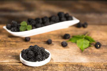 Ripe blackberries with leaves in a bowl on a woodenk background