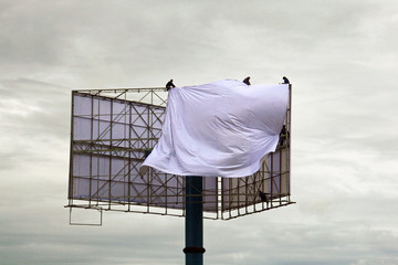 Vier Arbeiter spannen in luftiger Höhe an einer riesigen Werbetafel bei Hanoi, Vietnam eine...