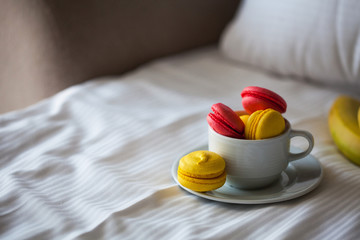 Fototapeta na wymiar Colorful French macaron pastries in a white circle on the white linen in bed. Red and yellow pasta.
