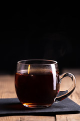  a transparent glass cup with hot tea stands on an old wooden surface on a black background with a place for inscription