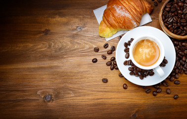Espresso and croissant with coffee beans on wood background. Top view
