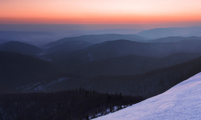 Fototapeta na wymiar Winter Carpathians. Morning twilight on mountain ridges covered with deciduous forest with orange sky on the horizon. Morning twilight in the winter Carpathians. Beskidy area.