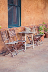 Fototapeta na wymiar Rustic wooden outdoor chairs and a table against orange wall