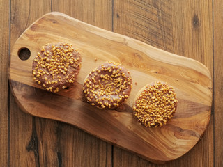 Three salted caramel doughnut with golden crumb on a wooden board and table.