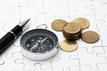 Compass,pen and coins on puzzle
