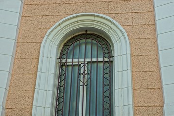 one large gray old window behind the iron bars against the brown concrete wall of the building