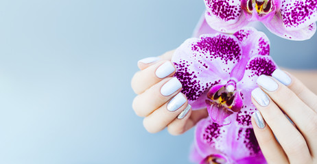 Beautiful hand with perfect nail pink manicure and purple orchid flower. on light blue background