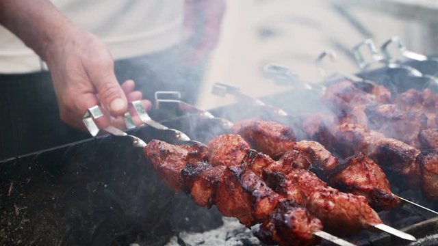 Turns a barbecue skewer on the grill. BBQ cooking. The smoke from the meat and fire. Picnic. Close-up, slow motion.