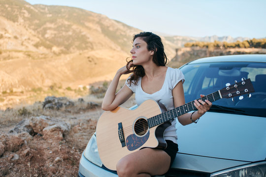 Woman playing the guitar in the field, leaning on her car. Green Summits, Granada, Spain.