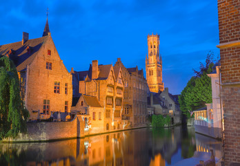 Famous view of Bruges tourist landmark attraction - Rozenhoedkaai canal with Belfry and old houses along canal with tree in the night. Belgium