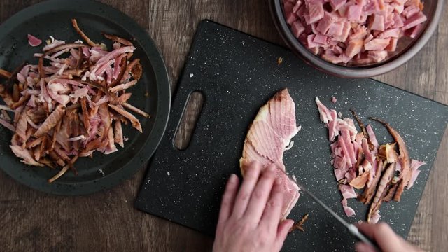 Woman&rsquo;s hands cutting cooked ham slices into small pieces for cooking