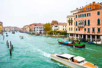 Fototapeta na wymiar Boats, yachts, vaporettos, water taxis sailing down the Grand Canal waterway between wooden and striped mooring poles and colorful Venetian architecture buildings. November in Venice city, Italy.
