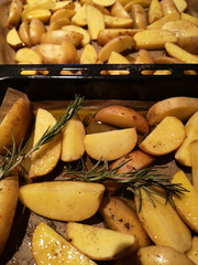 Geschnittene Kartoffelstücke mit Gewürzen auf einem Backblech in der Küche an Weihnachten in...