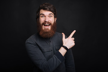 Amazed young bearded man pointing away at copyspace