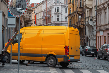 Fototapeta na wymiar Modern Yellow Delivery Truck Van In European Town At Cityscape Background