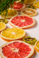 Fototapeta na wymiar Creative holiday Christmas New Year food fruit texture with dried grapefruit, kiwi, orange and lemon with branch of fir tree, angle view, white background, macro and selective focus