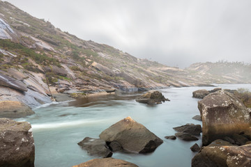 At the Ezaro waterfall, the water flows through the rocky valley towards the nearby Atlantic. The place is located in Galicia in northern Spain. Long exposure on a foggy winter morning.