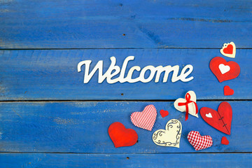 Welcome sign with red country hearts border hanging on antique rustic  blue wood door; Mothers Day and Valentines Day holiday background with painted copy space