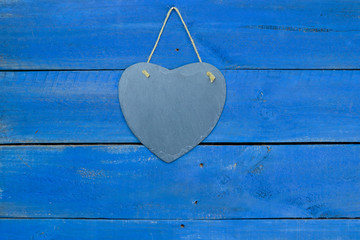 Blank slate heart sign hanging by rope on antique rustic blue wood door; Valentines Day holiday and love concept background with painted copy space