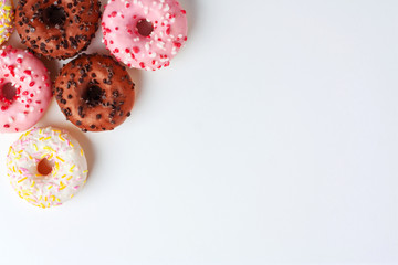 Colorful donuts with different glaze in the corner on white background close with copy space. Junk sweets.