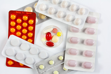 Tabletki w plastikowym pojemniku otoczone tabletkami w opakowaniach
