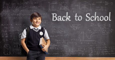 Schoolboy with a backpack standing in front of a blackboard with back to school text