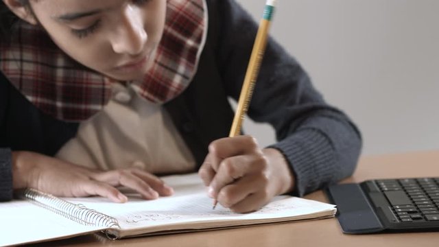 Latin brunette girl writing in notebook not her left hand focused on her homework.