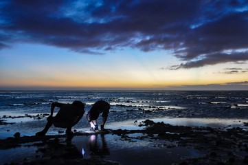 Boys wearing headlamps explore tide pools under a Fiji sunset