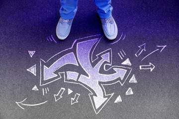 Person standing on asphalt road near arrows pointing in different directions, top view. Concept of choice