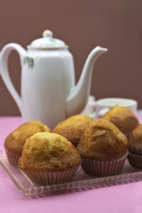 Muffins on a tray next to some cups of tea and a kettle