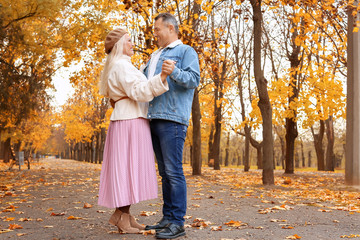 Fototapeta premium Happy mature couple dancing in autumn park among golden leaves, senior man and woman enjoying romantic date outdoors, active retirement lifestyle and love in fall