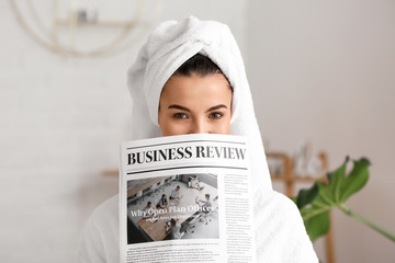 Beautiful young woman with newspaper in bathroom