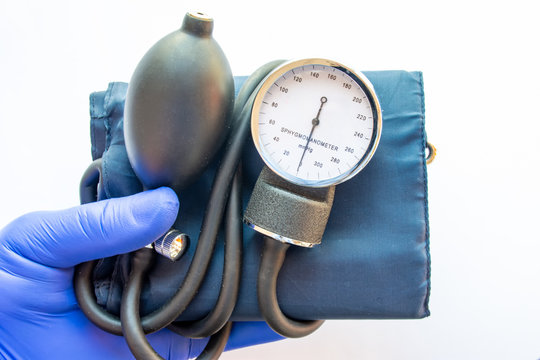 Medical professional, nurse or doctor holds in hand, wearing blue medical glove, blood pressure meter for measures blood pressure on white background. Concept for diagnosis of arterial hypertension