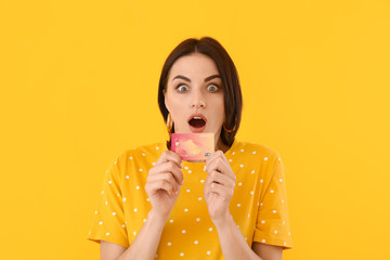 Beautiful surprised young woman with credit card on color background