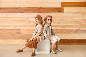 Cute little girls in autumn clothes near wooden wall