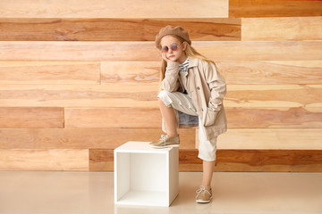 Cute little girl in autumn clothes near wooden wall