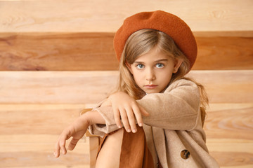 Cute little girl in autumn clothes sitting near wooden wall