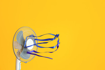 Electric fan with fluttering ribbons on color background