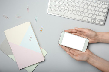 Obraz premium Female hands with mobile phone, PC keyboard and notebooks on light background
