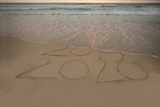 Year 2019-2020 message written on the sandy beach wave flashing at the background 