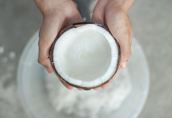 The hand is holding a half-cut coconut to scrape it into coconut milk for Thai cooking.