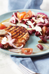 Grilled pork steak with Kidney bean, cherry tomatoes, onion and capers on bright wooden background