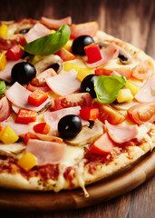Pizza with ham, cherry tomatoes, red and yellow pepper, black olives and fresh basil. 