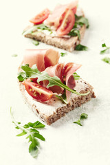 Tasty sandwiches with cream cheese, smoked ham and fresh herbs. Bright wooden background.