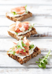 Tasty sandwiches with cream cheese, smoked ham and fresh herbs. Bright wooden background.